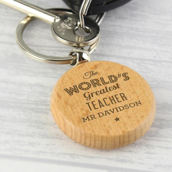 A round smooth beech wood keyring with a silver split ring, custom engraved with fixed uppercase text reading The World's Greatest Teacher Mr Evans.