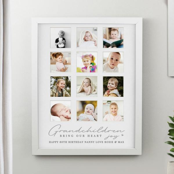 A large white multi-aperture picture frame mounted on a neutral wall, showcasing 12 family photos and a custom 80th birthday message for Nanny.