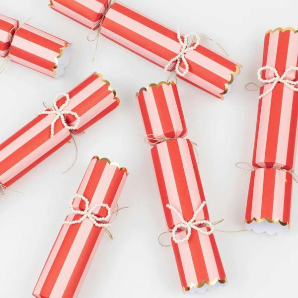 Scattered view of red and pink candy-striped Christmas crackers with faux pearl beaded bows and gold scalloped trim.