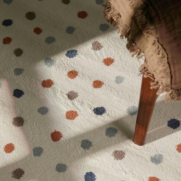 Close-up of a polka dot rug with a wooden chair leg and textured fabric corner.