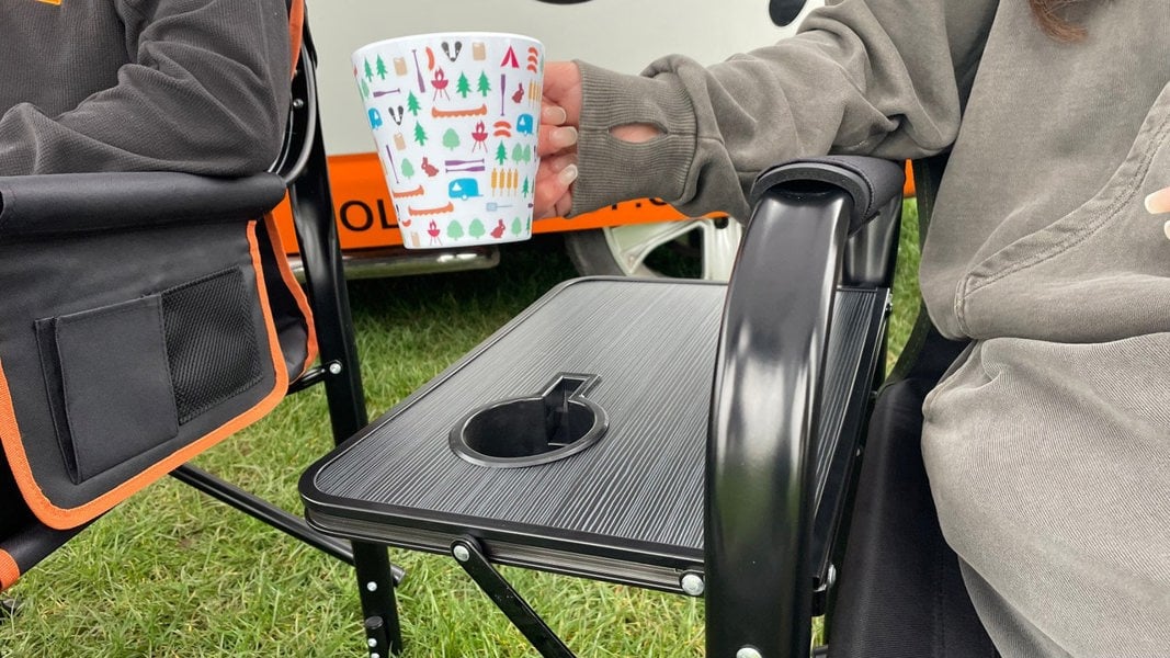 A closeup of a young female placing a melamine mug into the cupholder of the Directors Chair green and black.