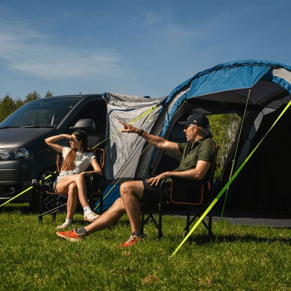 An image of a male and female pointing whilst sat outside of the Cocoon Breeze® v2 Campervan Awning from OLPRO on a volkswagen van, imageset:Blue