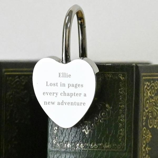 A silver-toned, heart-shaped metal bookmark hooked over the top of a green, vintage-style hardcover book. The bookmark is engraved with the text: "Ellie, Lost in pages, every chapter a new adventure".