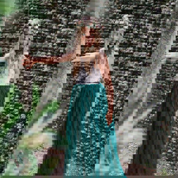 Girl in a white top and green skirt standing against a textured stone wall.