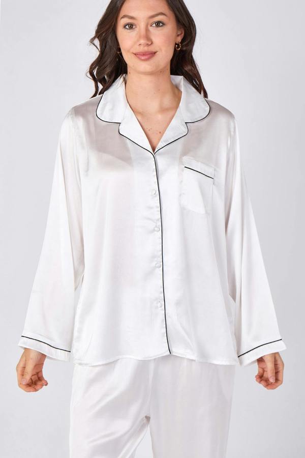Woman wearing white satin pajamas with black piping on a light gray background