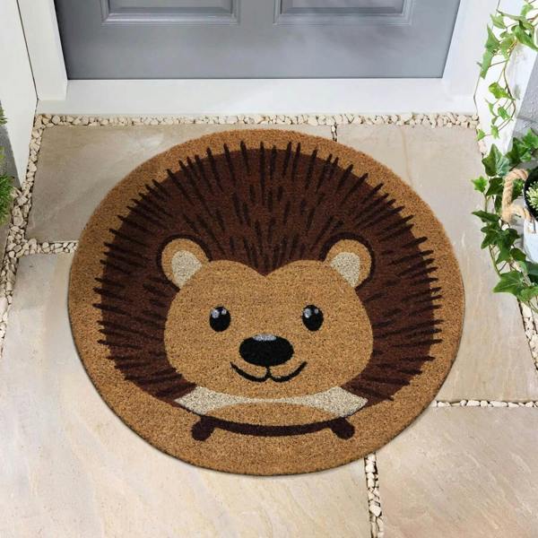 Round doormat with a hedgehog design on a stone pathway.