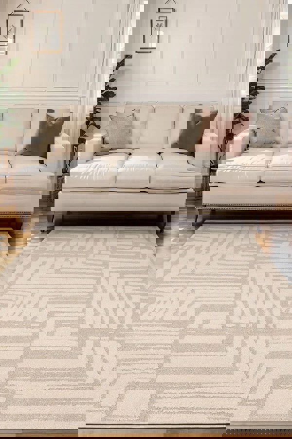 Ava Pave Wave Illusion Rug in cream tones, featuring an abstract design, placed in a modern living room with a beige sofa.