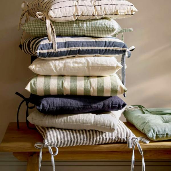 A stack of various solid and patterned linen seat pads on a wooden bench.