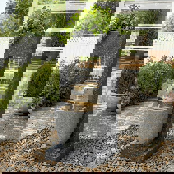 Sleek electric water feature with cascading water, gray stone finish, and a potted plant atop a rounded basin, enhancing outdoor tranquility