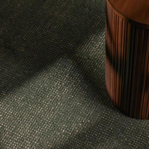Close-up of a textured green fabric surface with a wooden object corner.