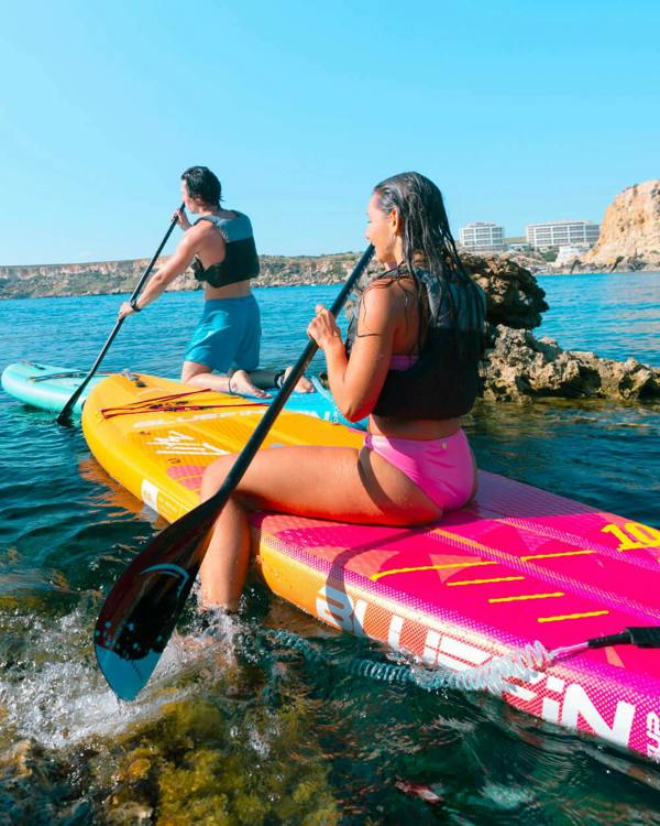 Man and woman sat on a Bluefin inflatable paddle board each from the Evolution Lite Series in the Malta ocean 