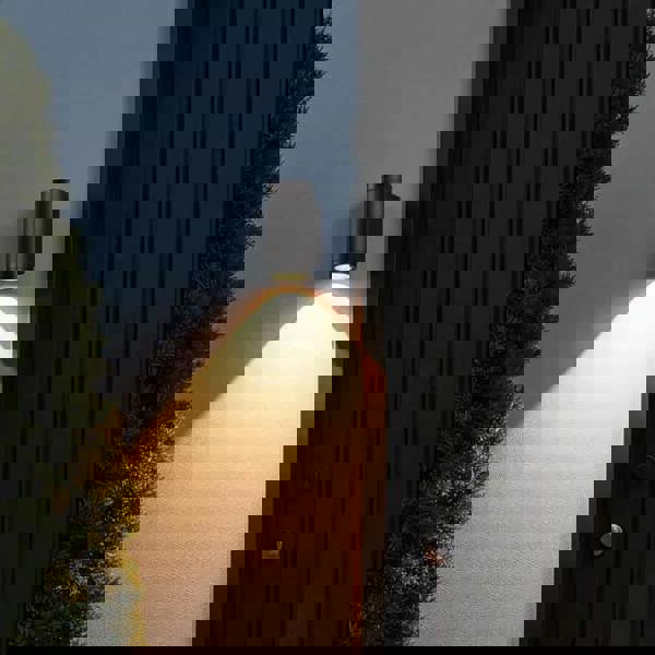 Black outdoor LED wall downlight mounted on a white wall next to a home front door