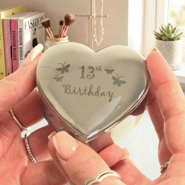 Abode Home & Gifts 13th Birthday engraved heart trinket box held in front of a bedroom vanity setup with fashion books, makeup brushes, and a jewellery stand.