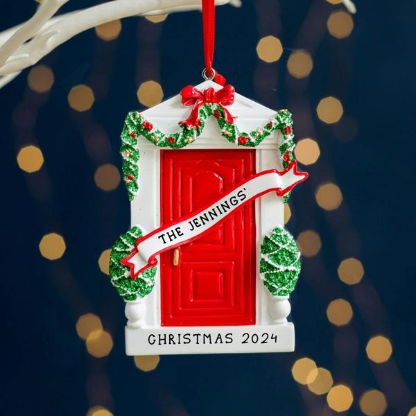 A personalised resin Christmas tree ornament shaped like a white doorway with a red door, festive garland, and a white scroll reading 'THE JENNINGS''.