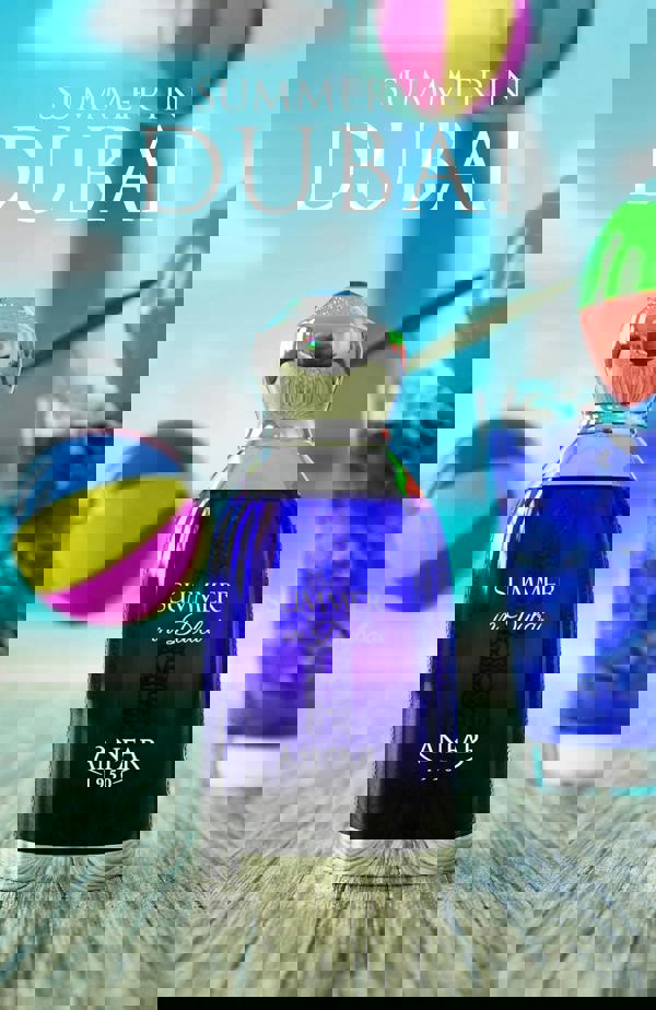 Blue perfume bottle labeled 'Summer in Dubai' by Anfar with beach balls and a glass of water in the background.