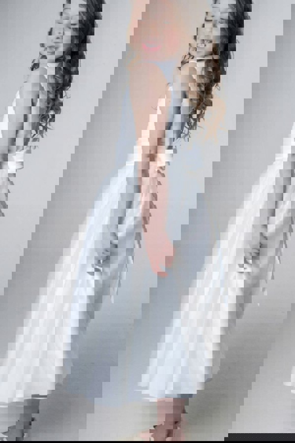 Young girl wearing a white dress with a belt on a plain background