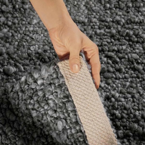 Hand holding a textured gray carpet sample against a matching carpet background