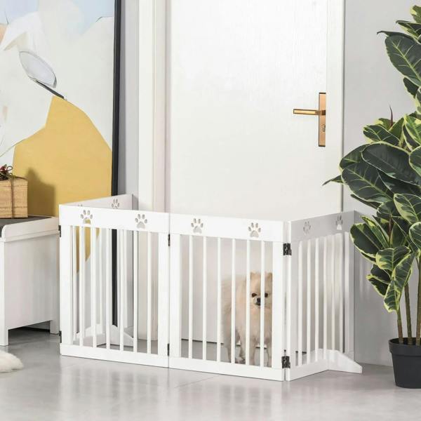 White folding pet gate with vertical bars and paw-print accents; small dog behind the barrier