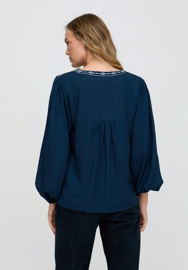 Woman wearing a navy blue blouse with intricate detailing on a plain background