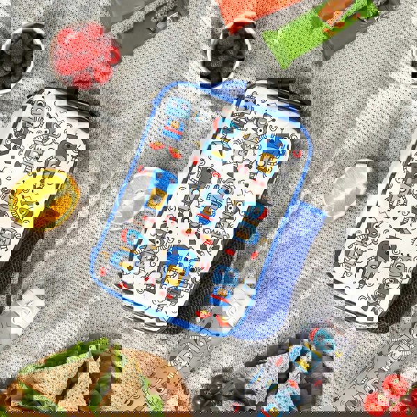 Lunchbox with cartoon robots resting on a picnic blanket surrounded by snacks including raspberries, an orange slice, sandwiches, granola bars, and a matching thermos featuring the same robot pattern.