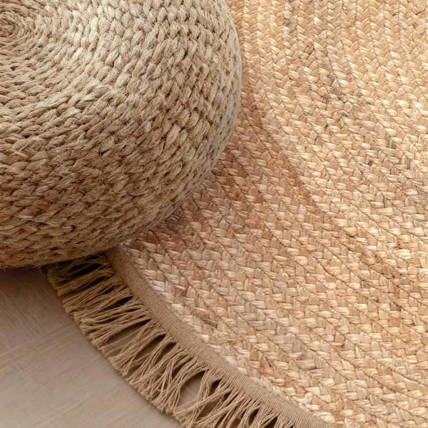 Close-up of a woven rug with a textured ottoman on a wooden floor.