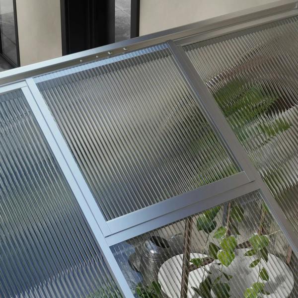 Close-up of sloped clear polycarbonate roof panel on aluminium greenhouse frame.