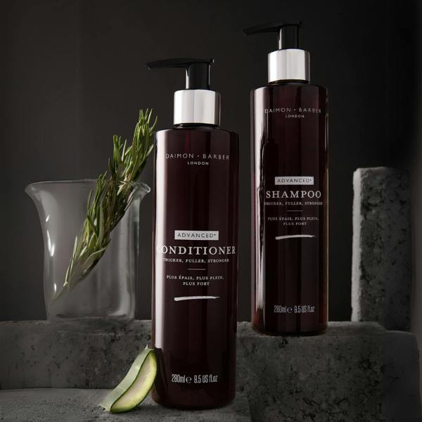 Bottle of Advanced+ Shampoo and Conditioner in darkly lit shot with rosemary and aloe vera.
