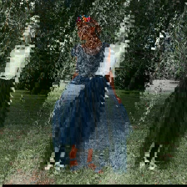 Young girl in a white top and navy blue skirt standing in a grassy area with trees.