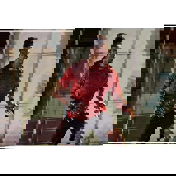 Man in red athletic shirt and black shorts exercising outdoors with the 1.5kg adidas wrist weights