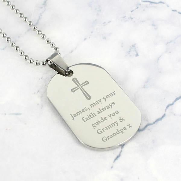 Personalised stainless steel dog tag necklace with a small engraved cross and a custom blessing message on a white marble background.