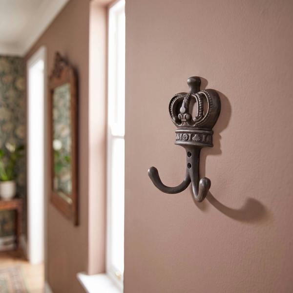 Cast iron twin coat hook with coronation crown design mounted on vintage painted wall in hallway.