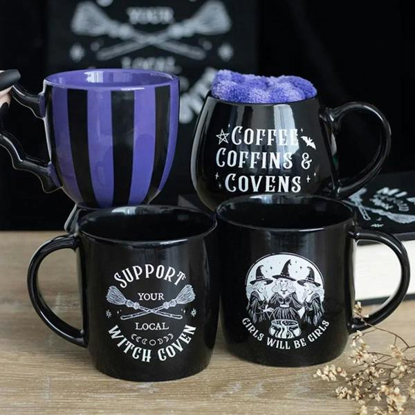 Assorted black coffee mugs on wood, one says 'Support Your Local Witch Coven'