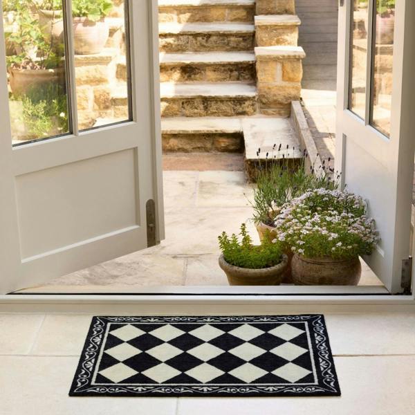 Decorative checkered mat in front of a glass door with plants and steps outside.
