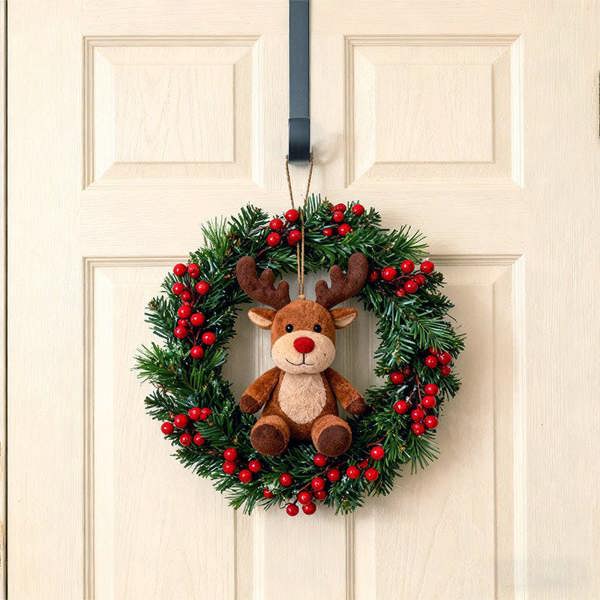 Christmas wreath with a plush reindeer toy hanging on metal hook over a door.