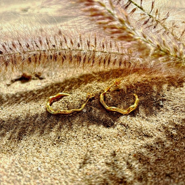 Gold vermeil hoops with a wavy design, displayed on the beach