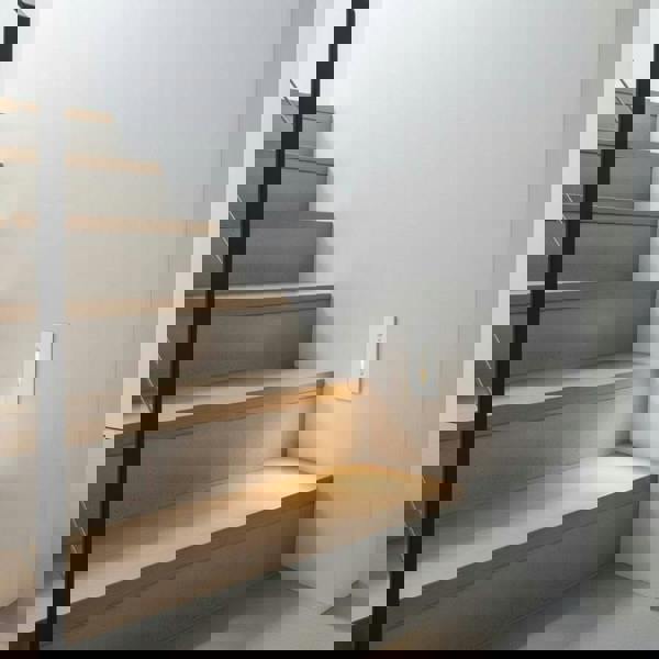 white motion sensor step light installed at the bottom of a staircase on the wall 