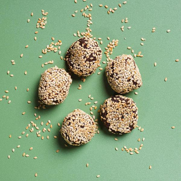Five sesame seed balls on a green background with scattered sesame seeds.