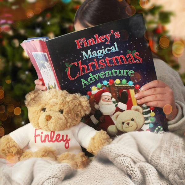 A personalised festive children's storybook open on a white surface, displayed next to a grey plush teddy bear wearing a white custom t-shirt.