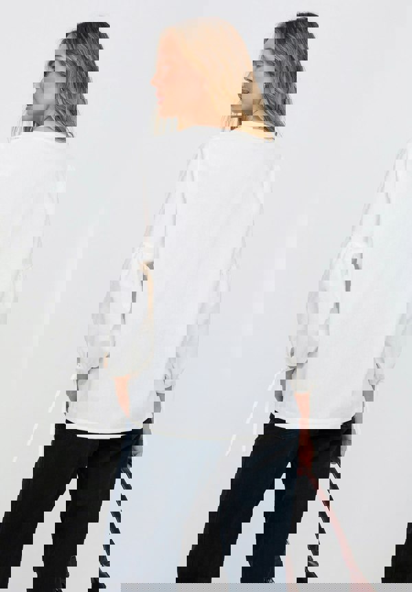 Woman wearing a white blouse and dark pants against a plain background