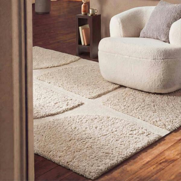 Beige textured rug on a wooden floor with a white armchair in the corner.