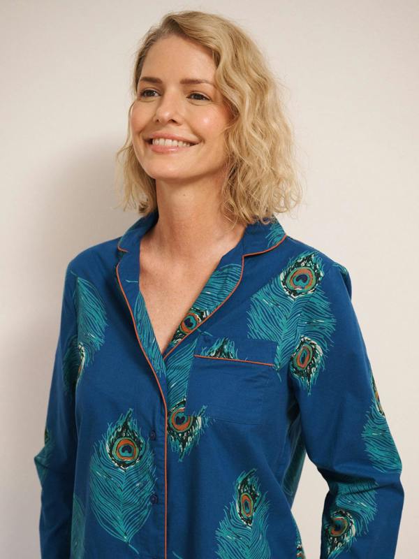 Woman wearing a blue pyjama shirt with peacock feather patterns on a plain background