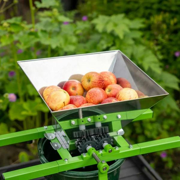 Stainless steel fruit crusher with a large hopper filled with red apples, mounted on a green frame for easy pressing