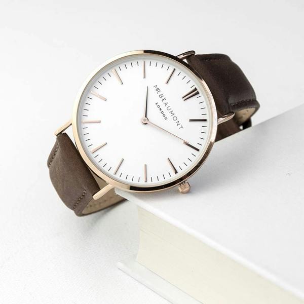 A Mr Beaumont men's wristwatch with a genuine brown leather strap and a large white face with rose gold-plated hour markers and hands. The watch is resting on a white book