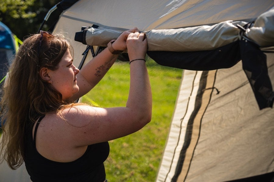 A young woman rolls up the front door & fly mesh on an  OLPRO Cubo  poled Campervan Awning