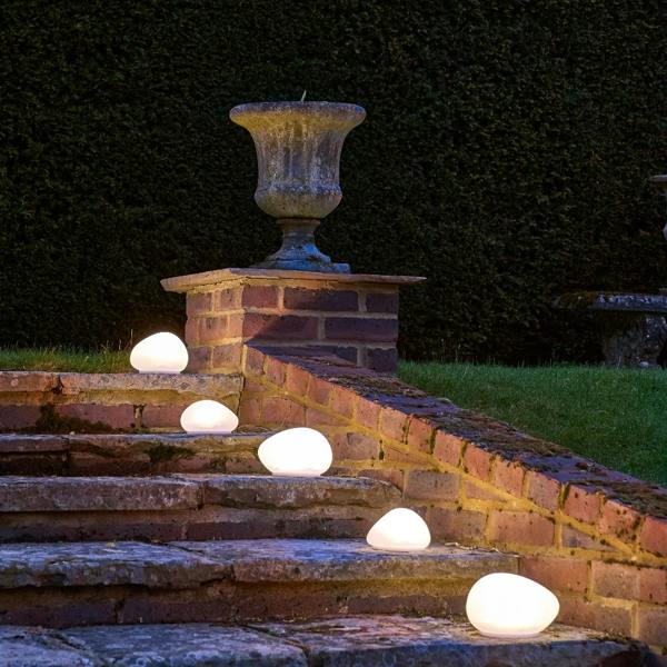 A line of frosted glass solar pebble lights illuminating one side of brick and stone garden steps at dusk near a stone urn planter.