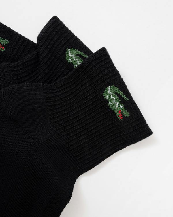 Black ribbed knit socks with green crocodile logos and small red accents on the cuffs, shown on a plain white background.
