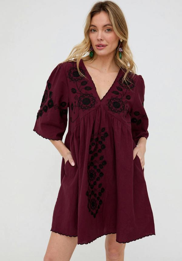 Woman wearing a burgundy dress with black embroidery on a white background