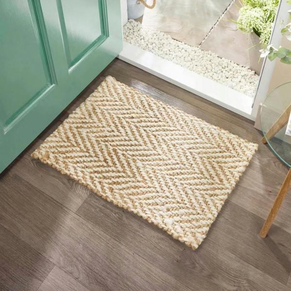 Beige doormat with a zigzag pattern on a wooden floor in front of a green door.