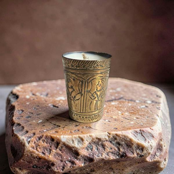 Decorative candle in an ornate brass holder on a stone surface with a brown background