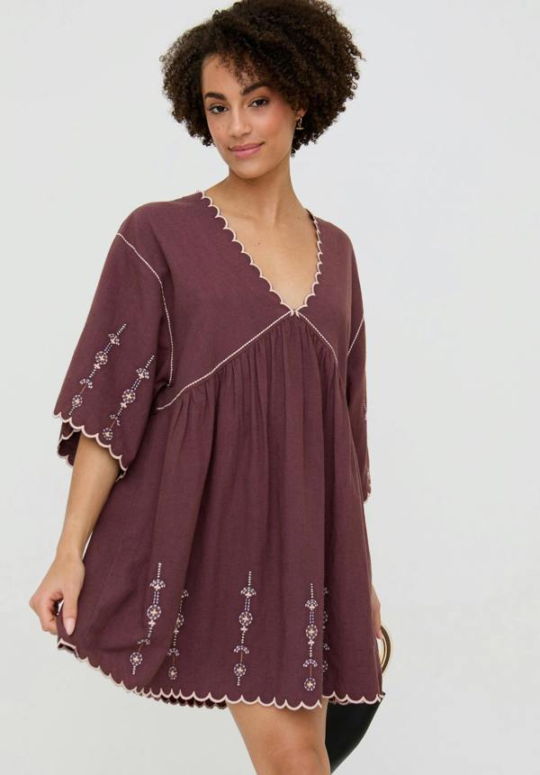 Woman wearing a burgundy dress with white embroidery on a plain background